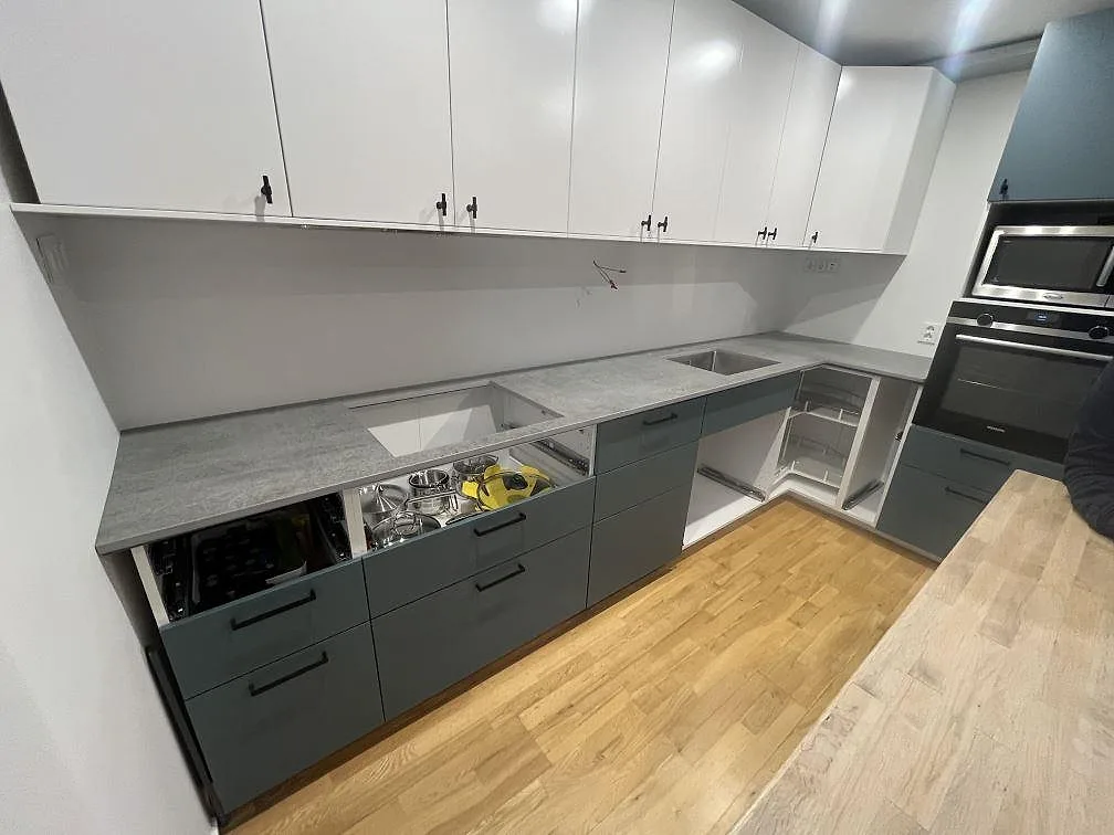 L-format køkken med ljusgrå køkkenbordplade i mat Dekton Kreta, sintrad keramik, monteret på grå köksstommar i Skogås.