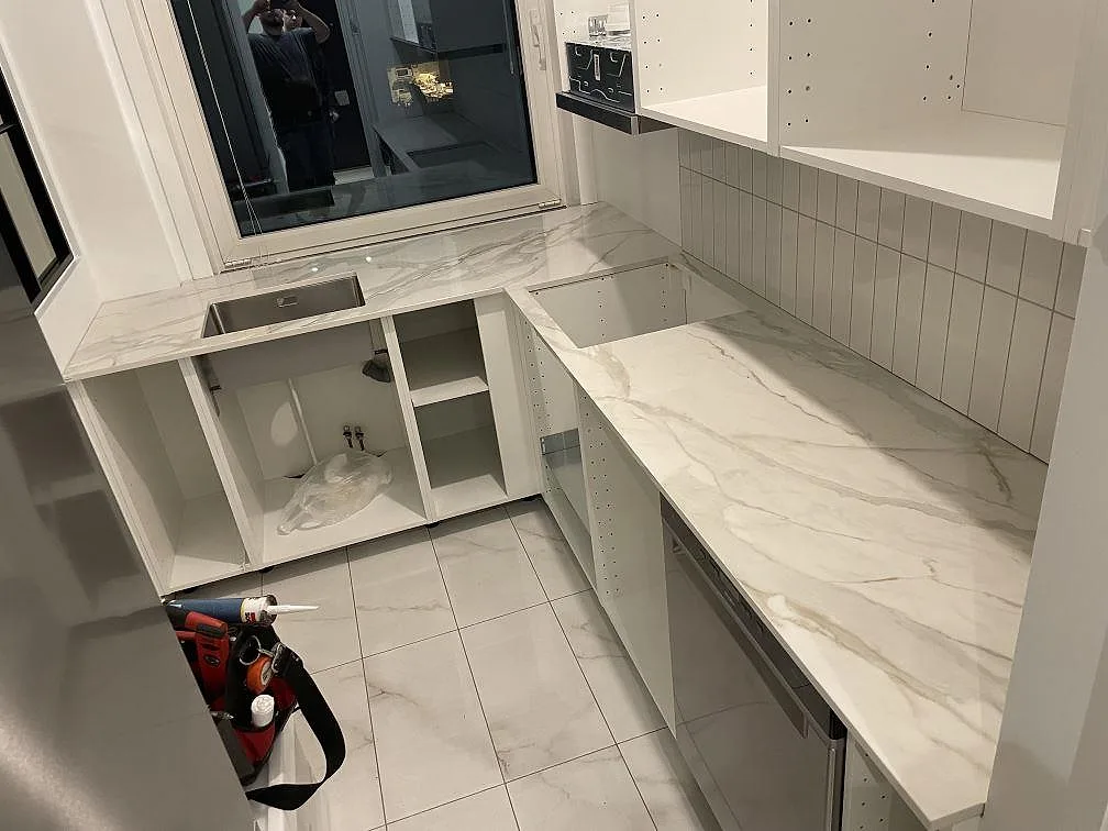 Køkkenbordplade i hvid marmorerad Dekton Lucid, poleret, monteret längs väggarna i ett køkken i Stockholm.