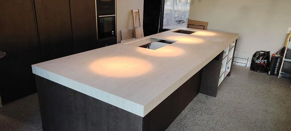 Stor køkkenø med Bordplade i hvid Dekton Marmorio, mat keramik, med hällområde og blød marmorådring i ett køkken i Värmdö.