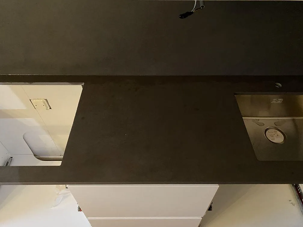 Køkkenbordplade i mørk mat Dekton Micron keramik med synlig vask og udskæring i ett køkken under montering i Bunkeflostrand.