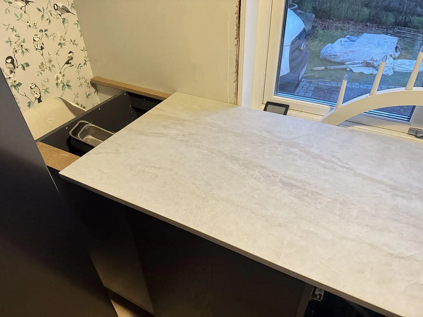 Køkkenbordplade i hvid Dekton Nara, mat keramik, monteret vid ett vindue med uppvikt stänkkant i ett køkken under montering i Halmstad.