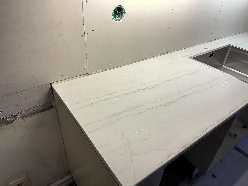 Køkkenbordplade i lys Dekton Neural, mat keramik, med grå åretegning og rostfri vask under montering i Lund.