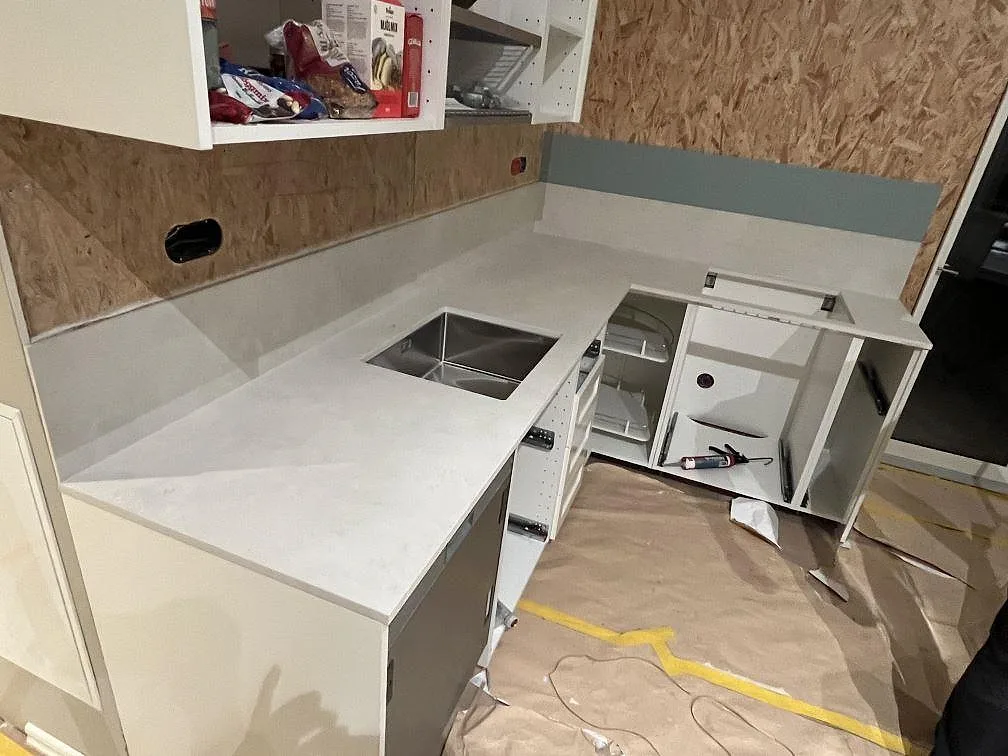 Køkkenbordplade i lys Dekton Sandik, mat, med stænkplade og synlig vask under montering i Värmdö.