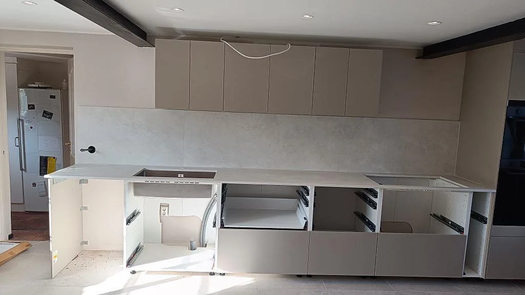 Køkkenbordplade og stænkplade i mat Dekton Sandik keramik, monterade längs en köksvägg med vask og öppna skabe i Vellinge.