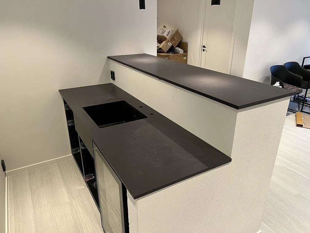 Køkkenbordplade i mørk mat Dekton Sirius, keramik, med hälluttag og upphöjd bänkdel i ett køkken i Trosa.