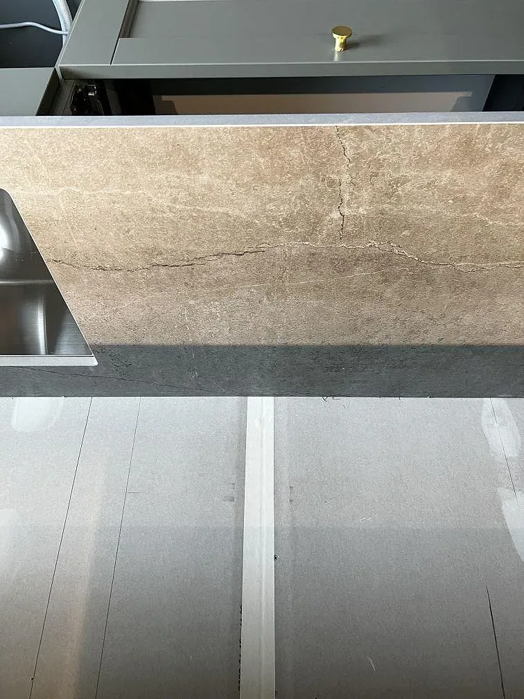 Køkkenø i mat beige Dekton Soke med infälld induktionshäll i ett køkken under montering i Uddevalla.