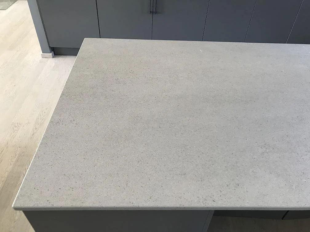Køkkenbordplade i ljusgrå Dekton Strato, mat overflade, på en køkkenø mot grå köksluckor i ett køkken i Rydebäck.