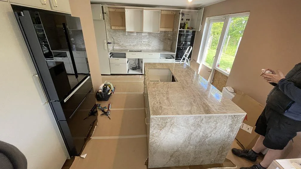 Køkkenø og väggbänkar i poleret Dekton Taga keramik med gråbeige åretegning under montering i ett køkken i Anderslöv.