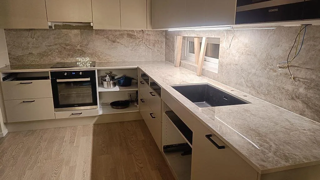 Køkkenbordplade i varmgrå Dekton Taga, poleret, i ett L-format køkken med heltäckande stänkvägg, underlimmad sort komposithon og infälld induktionshäll i Borås.
