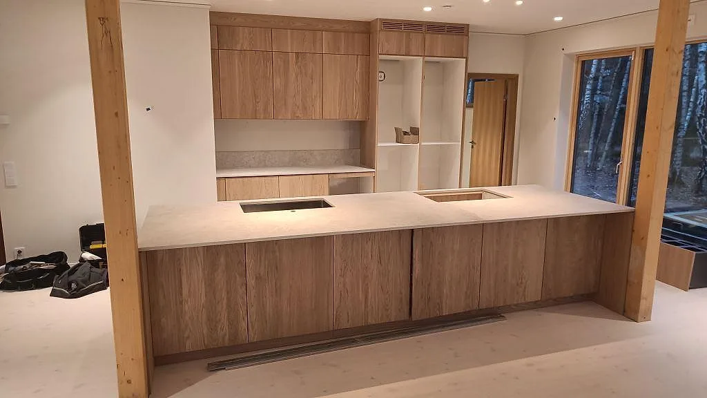 Køkkenbordplade og køkkenø i mat Dekton Tk05 Sabbia, beige keramik, med udskæring for kogeplade og vask i ett køkken i Höllviken.