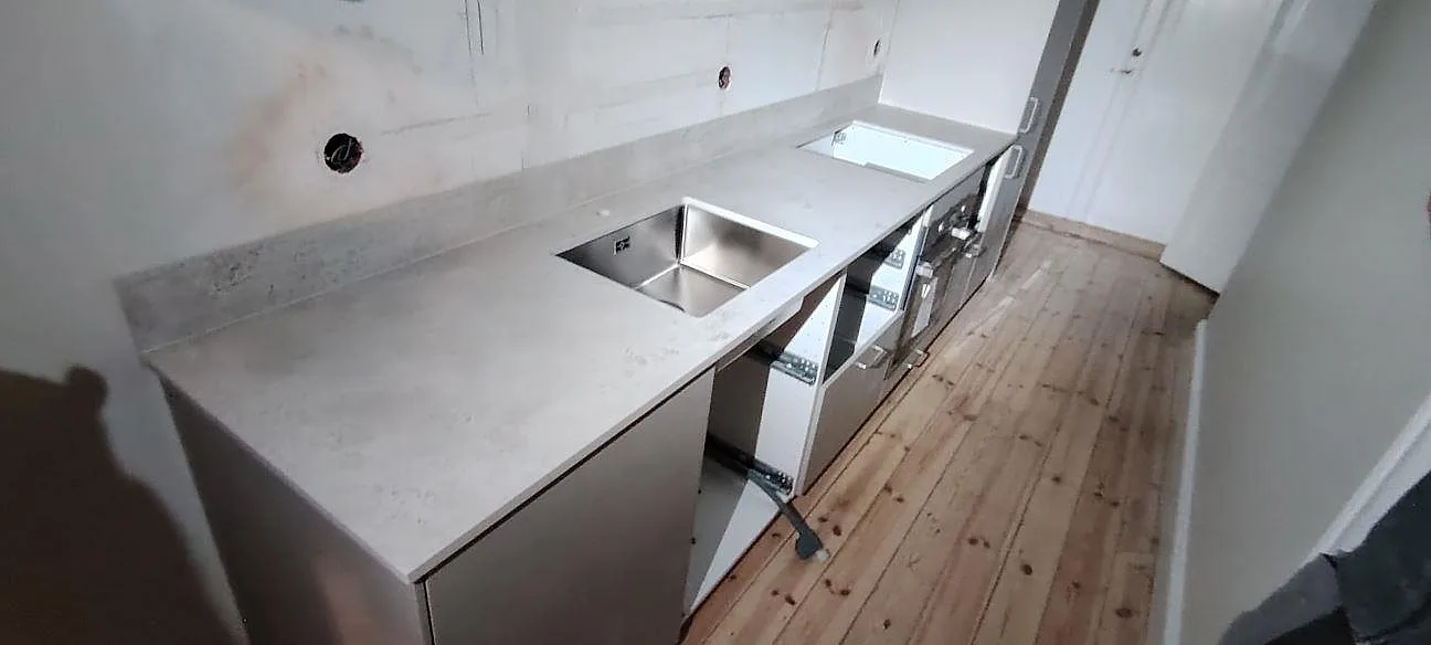 Køkkenbordplade i lys beige Dekton Tk05 Sabbia, mat, med underlimmad vask og stænkplade under montering i Stockholm.