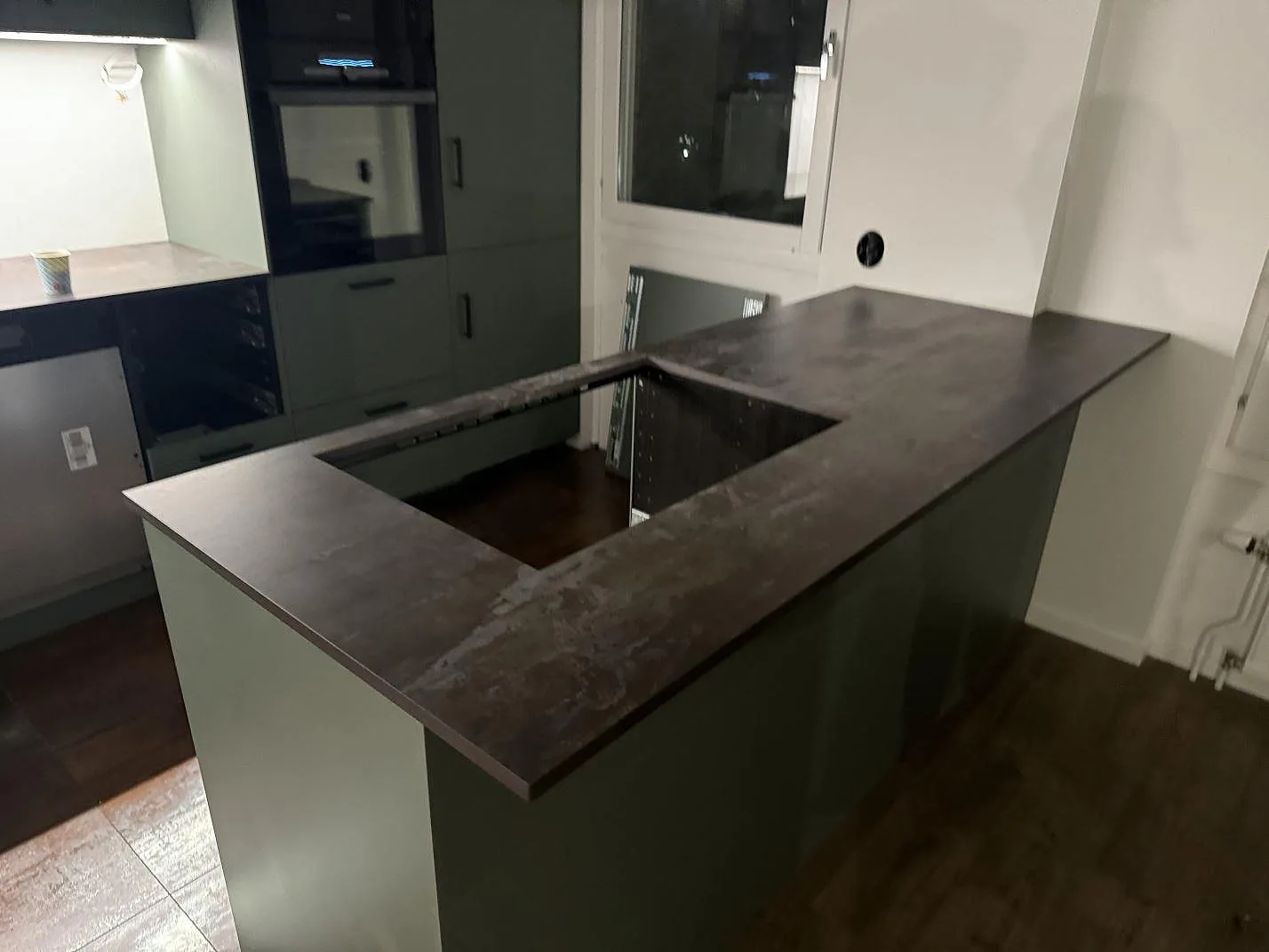 Køkkenø med køkkenbordplade i mat Dekton Trilium, mørk keramisk overflade og större urtagning i ett køkken i Helsingborg.