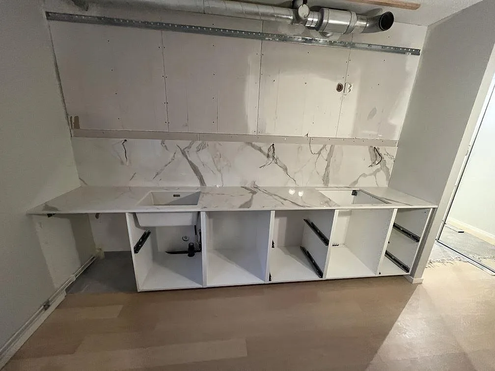 Køkkenbordplade i vitmarmorerad Dekton Vigil, poleret keramik, med stænkplade og grå åretegning i ett køkken under montering i Stockholm.