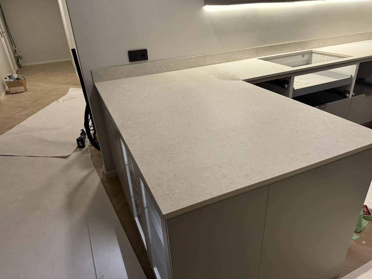 Køkkenbordplade i mat Dekton VK01 Nebbia med lys ådrad overflade, 8 mm stænkplade og köksstommar under montering i Trelleborg.
