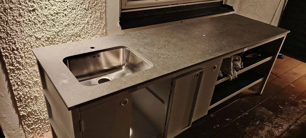 Køkkenbordplade i mat Dekton Vk04 Grafite, 20 mm keramik, på mørke utomhusstommar med synlig rostfri vask i Tyresö.