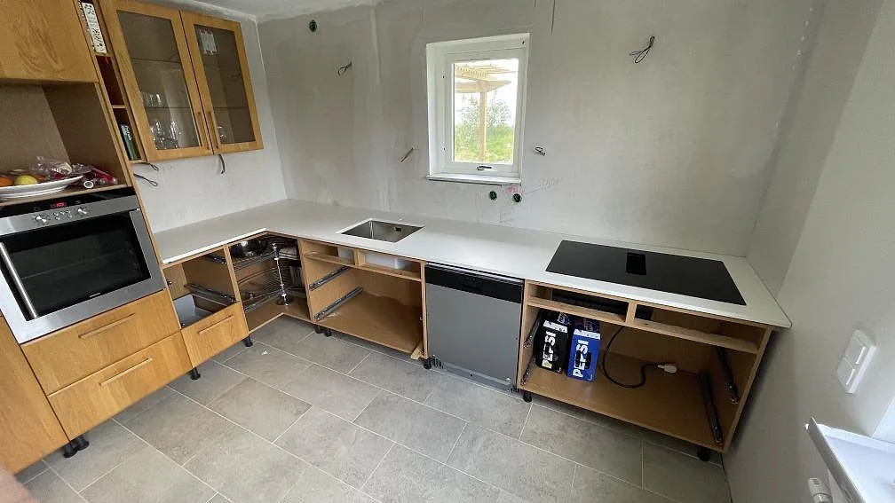 Køkkenbordplade i mat Dekton Zenith, lys keramik, med rostfri vask og sort kogeplade i ett køkken under montering i Höör.