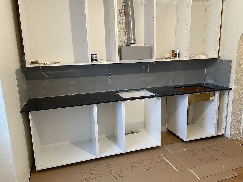Køkkenbordplade i mørk skimrande Emerald Pearl-granit, poleret, monteret längs en væg med urtagning for vask og kogeplade i ett køkken under montering i Malmö.