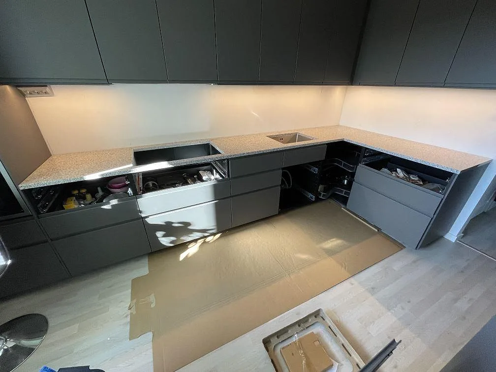 Køkkenbordplade i Grigio Cristallo granit, poleret, monteret i ett L-format køkken med mörkgrå skabe i Nacka.