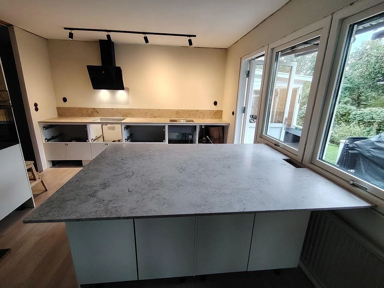 Køkken i Enköping med køkkenø og väggbänk i mat Jura Grey, 20 mm, med låg stänkkant längs væggen.