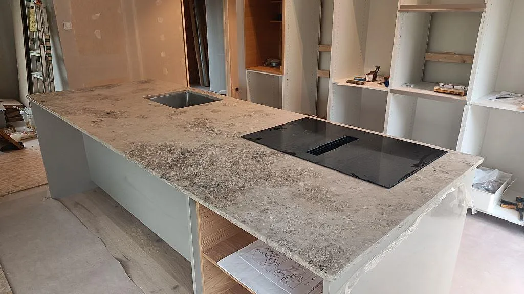 Køkkenbordplade i mat Jura Grey på køkkenø med rostfri vask og sort kogeplade i ett køkken i Marstrand.