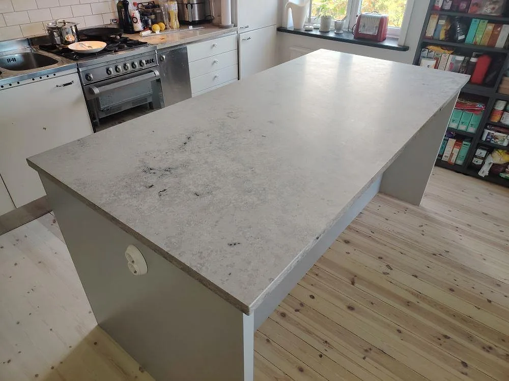 Köksöskiva i mat Jura Grey kalksten, 30 mm, monteret som bred arbetsyta i ett køkken med fristående komfur og trägolv i Stockholm.