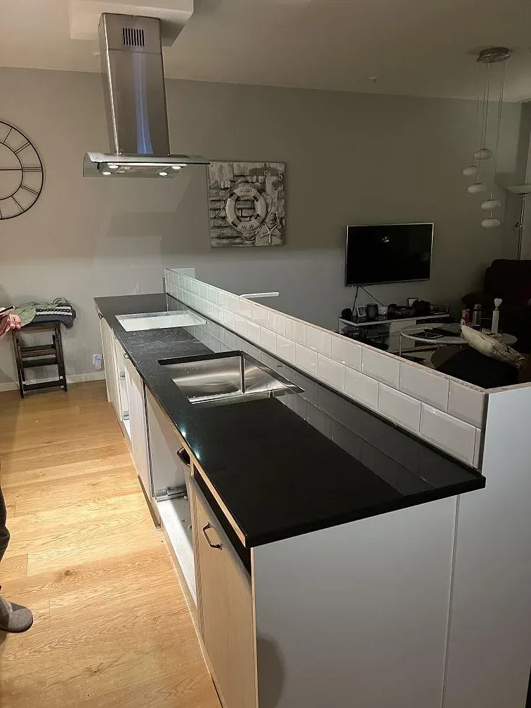 Køkkenbordplade i poleret sort granit Nero Assoluto, monteret längs lys köksinredning i Åkersberga.