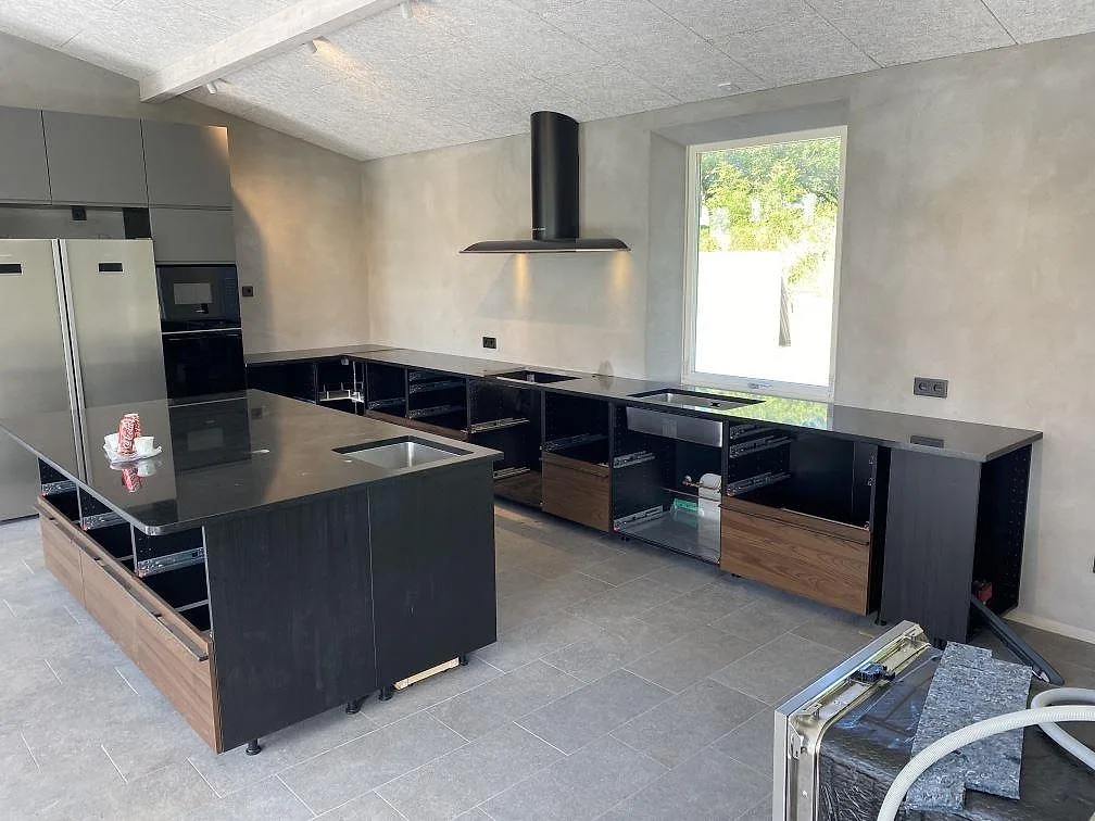 Översikt af køkken i Båstad med poleret køkkenbordplade i Nero Assoluto granit på väggbänkar og køkkenø under montering.