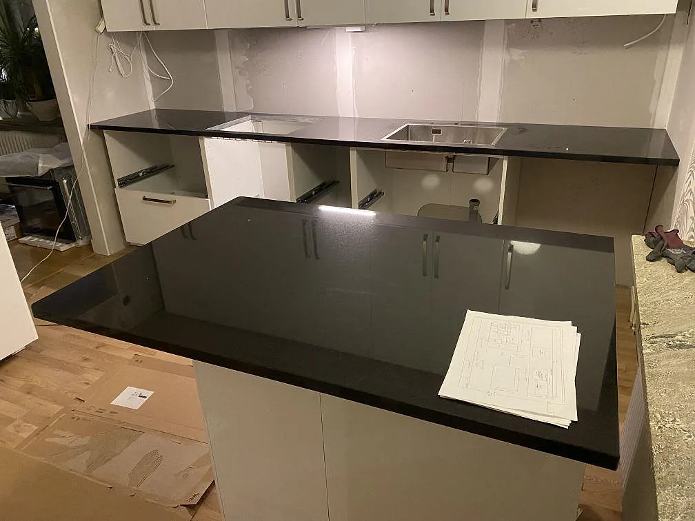 Køkkenbordplader og køkkenø i 30 mm poleret Nero Assoluto granit med rostfri vask i ett køkken under montering i Hässleholm.