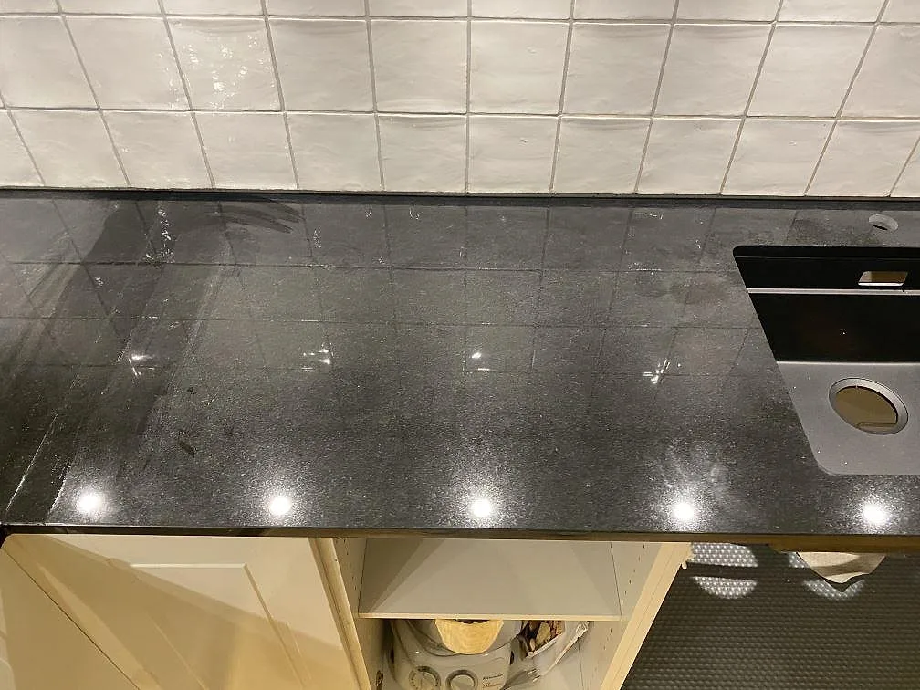 Køkkenbordplade i poleret Nero Assoluto-granit med underlimmad sort kompositdiskho mot vitt kakel i ett køkken i Lomma.