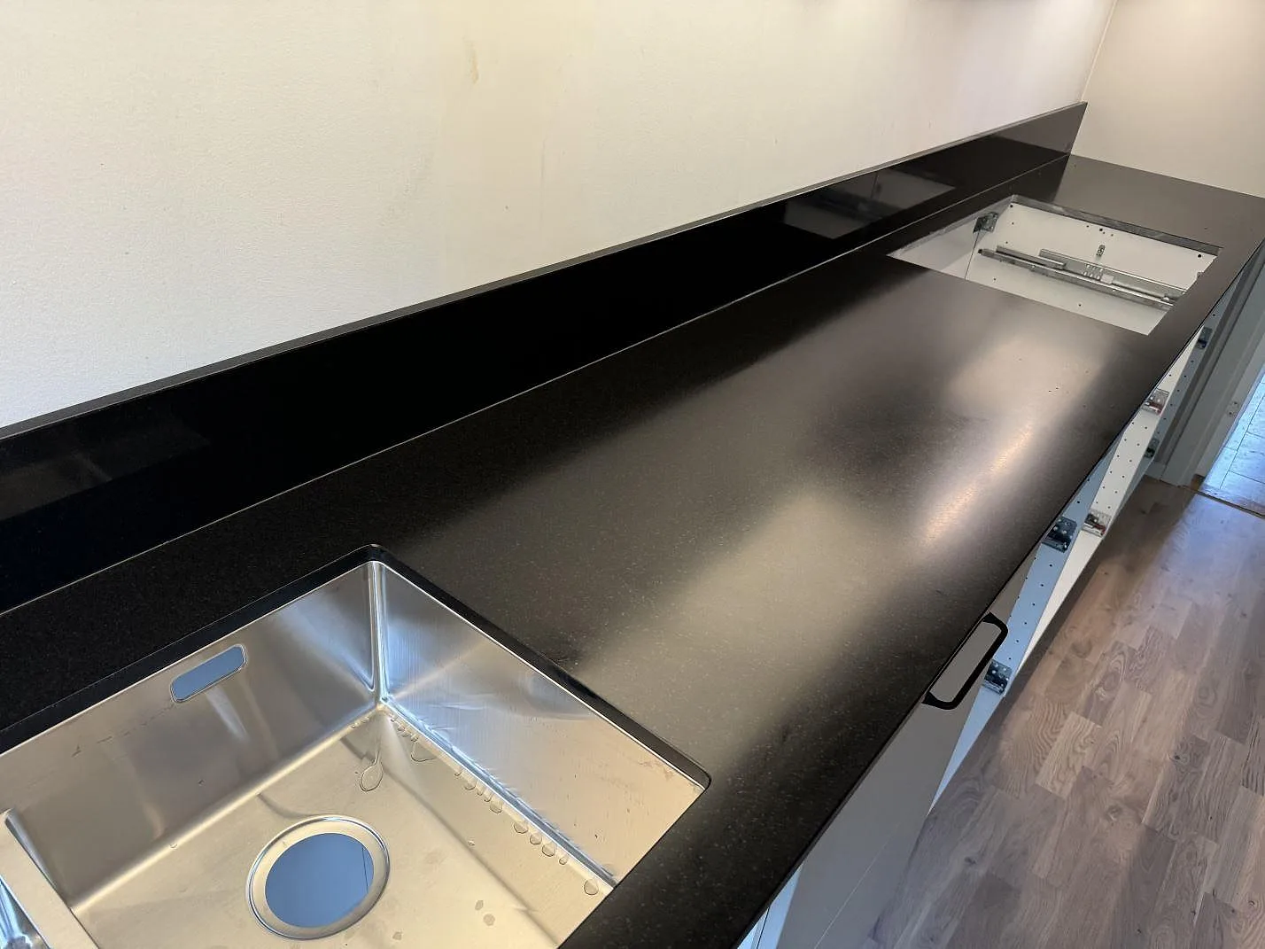 Køkkenbordplade i mat Nero Assoluto granit med låg sort stänkkant og synlig rostfri vask i ett køkken i Lomma.