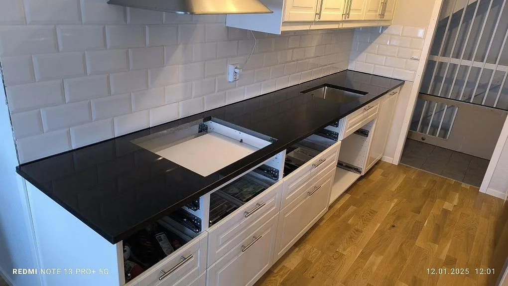 Køkkenbordplade i sort poleret Nero Assoluto granit, 30 mm, längs en hvid kakelvägg i ett køkken i Motala.