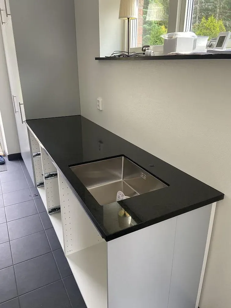 Køkkenbordplade i sort Nero Assoluto, poleret granit, med underlimmad rostfri vask og vindue i bakgrunden i ett køkken i Saxtorp.