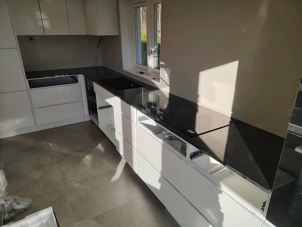 Køkkenbordplade i 20 mm sort Nero Assoluto granit, poleret, monteret längs vita köksstommar i ett køkken i Stora Skedvi.