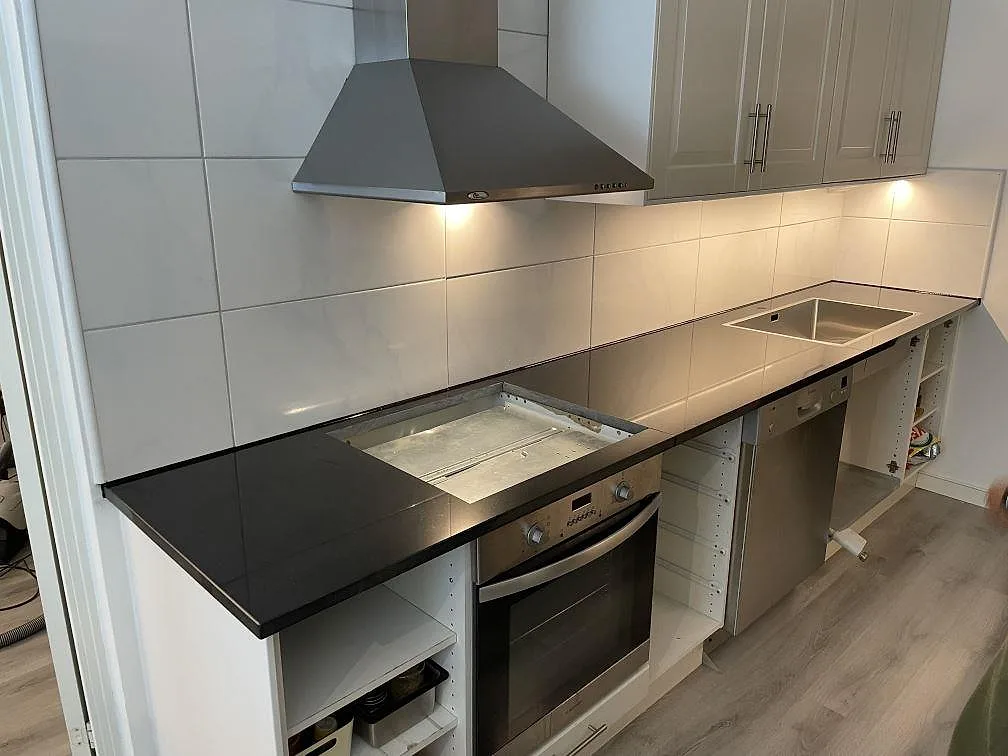 Lige køkkenbordplade i 30 mm poleret Nero Assoluto granit längs hvid kakelvägg i ett køkken i Täby.