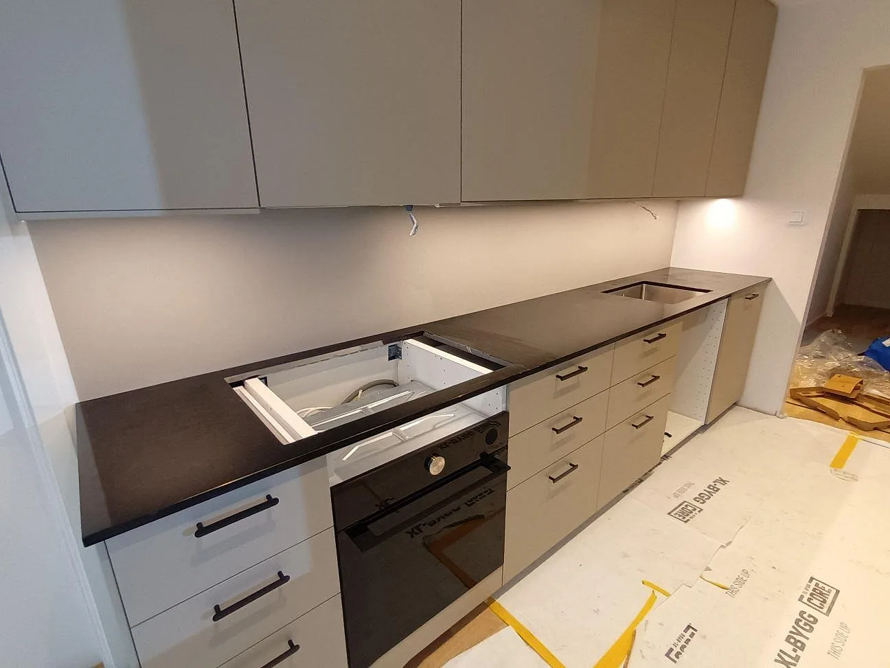 Køkkenbordplade i sort granit Nero Assoluto, poleret, längs en lang köksvägg med udskæring for vask og kogeplade under montering i ett køkken i Vällingby.
