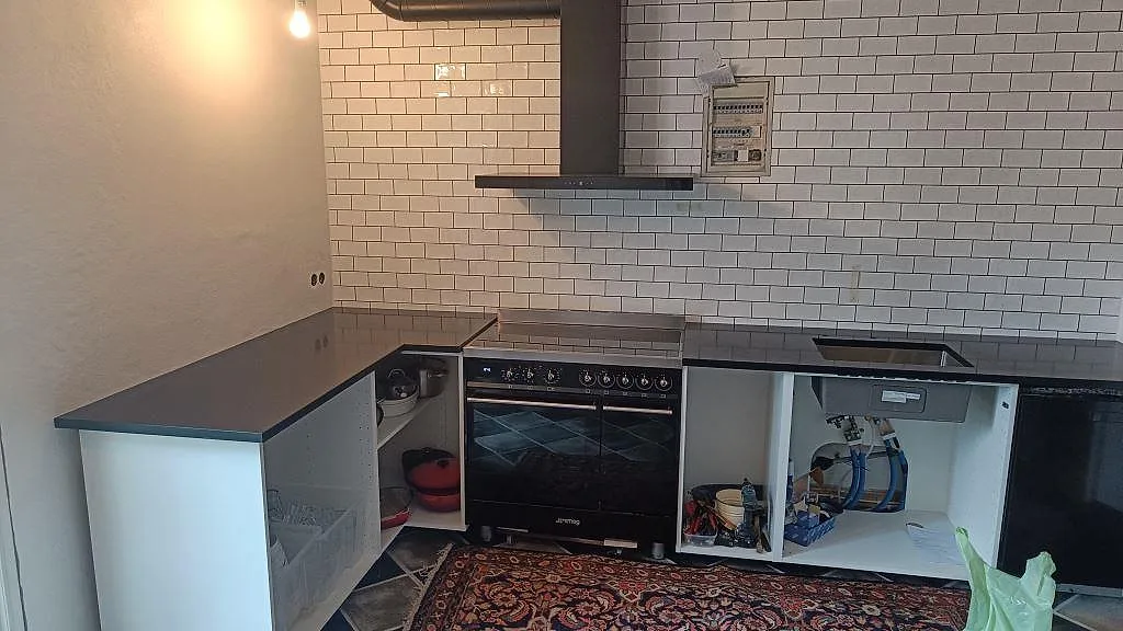 Køkkenbordplade i mat Nero Assoluto granit med rostfri vask og fristående komfur i ett køkken i Ystad.
