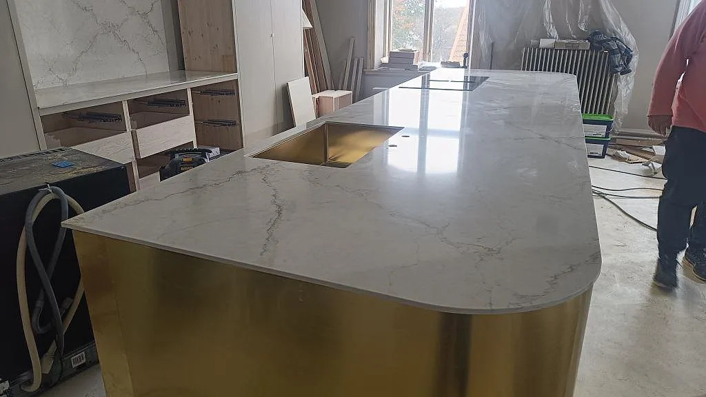 Køkkenø med Bordplade i poleret Silestone Blanc Elysee, hvid kvartskomposit med grå åretegning, kogeplade og mässingsfärgad vask i Allerum.