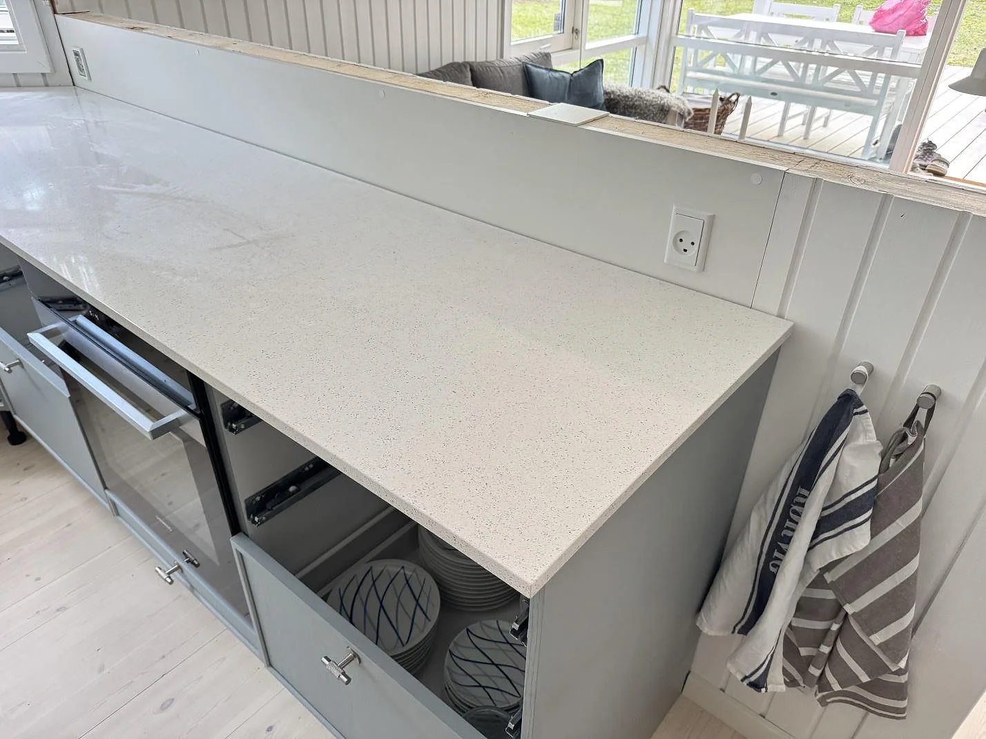 Køkkenbordplade i lys Silestone Blanco Maple 14, poleret kvartskomposit, längs en lang lige bordplade med öppna skabe under montering i ett køkken i Rørvig.