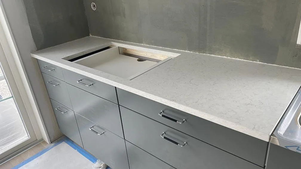 Køkkenbordplade i lys Silestone Blanco Orion, poleret kvartskomposit med fint grått stänk, med underlimmad vask og separat borrat Armaturhul under montering i ett køkken i Nol.