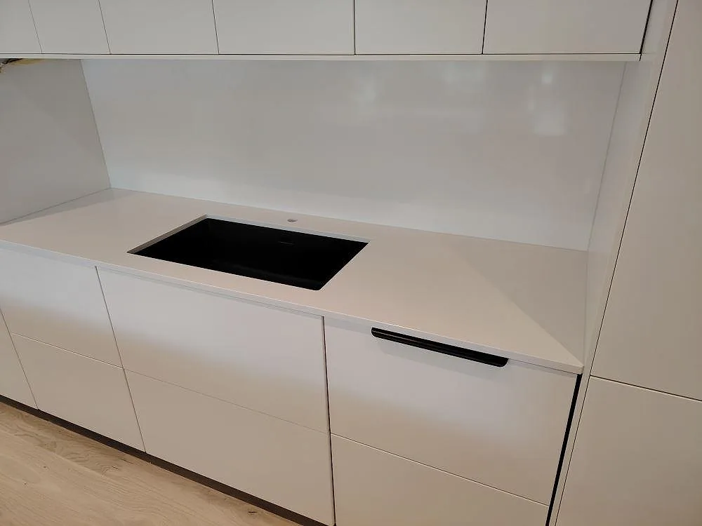 Väggbänk i hvid Silestone Blanco Zeus, poleret kvartskomposit, med sort kogeplade og matchande stænkplade i ett køkken i Västerås.
