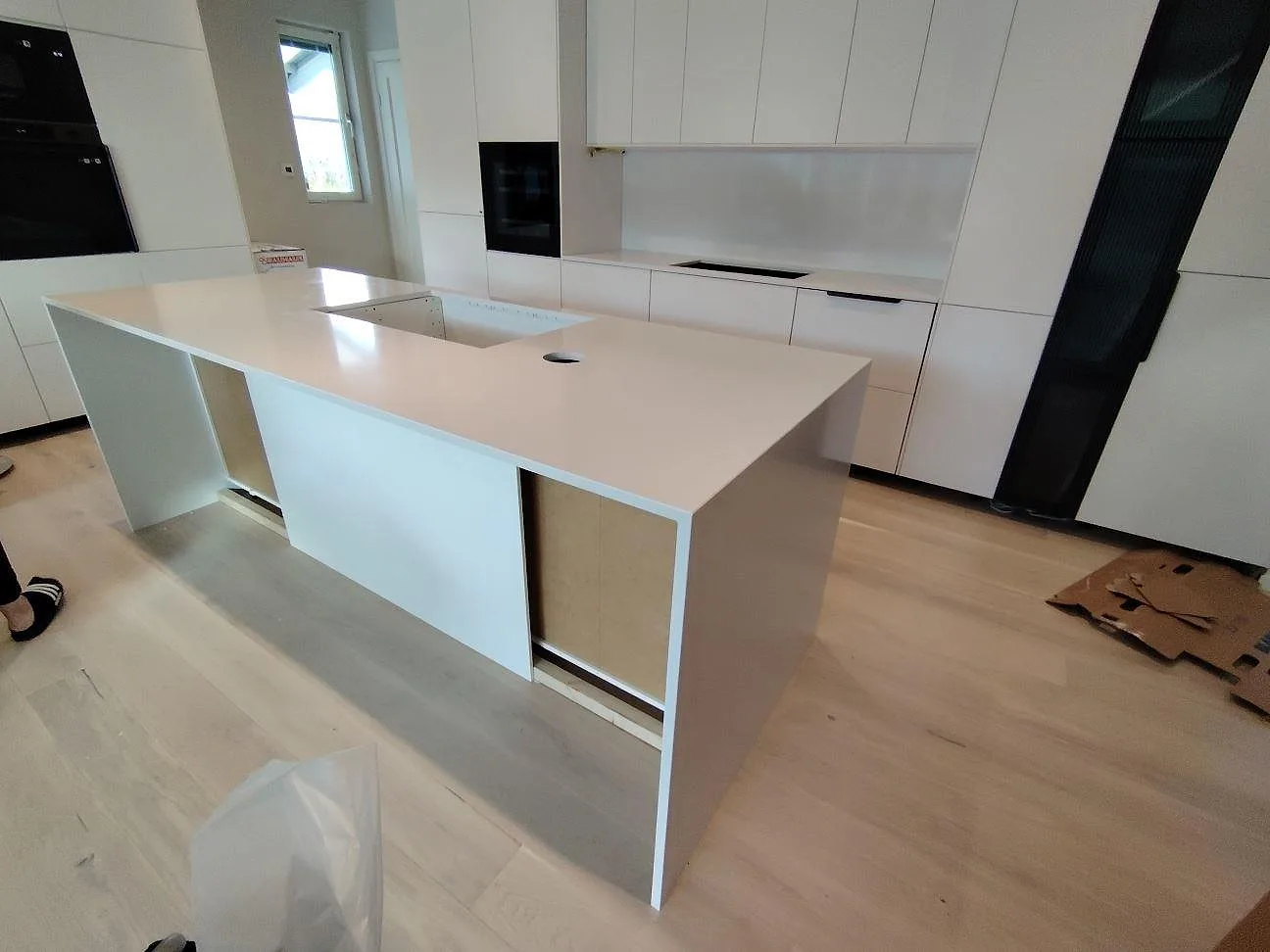 Køkkenbordplade og køkkenø i hvid Silestone Blanco Zeus, poleret kvartskomposit, med sort kogeplade og stænkplade i ett køkken i Västerås.