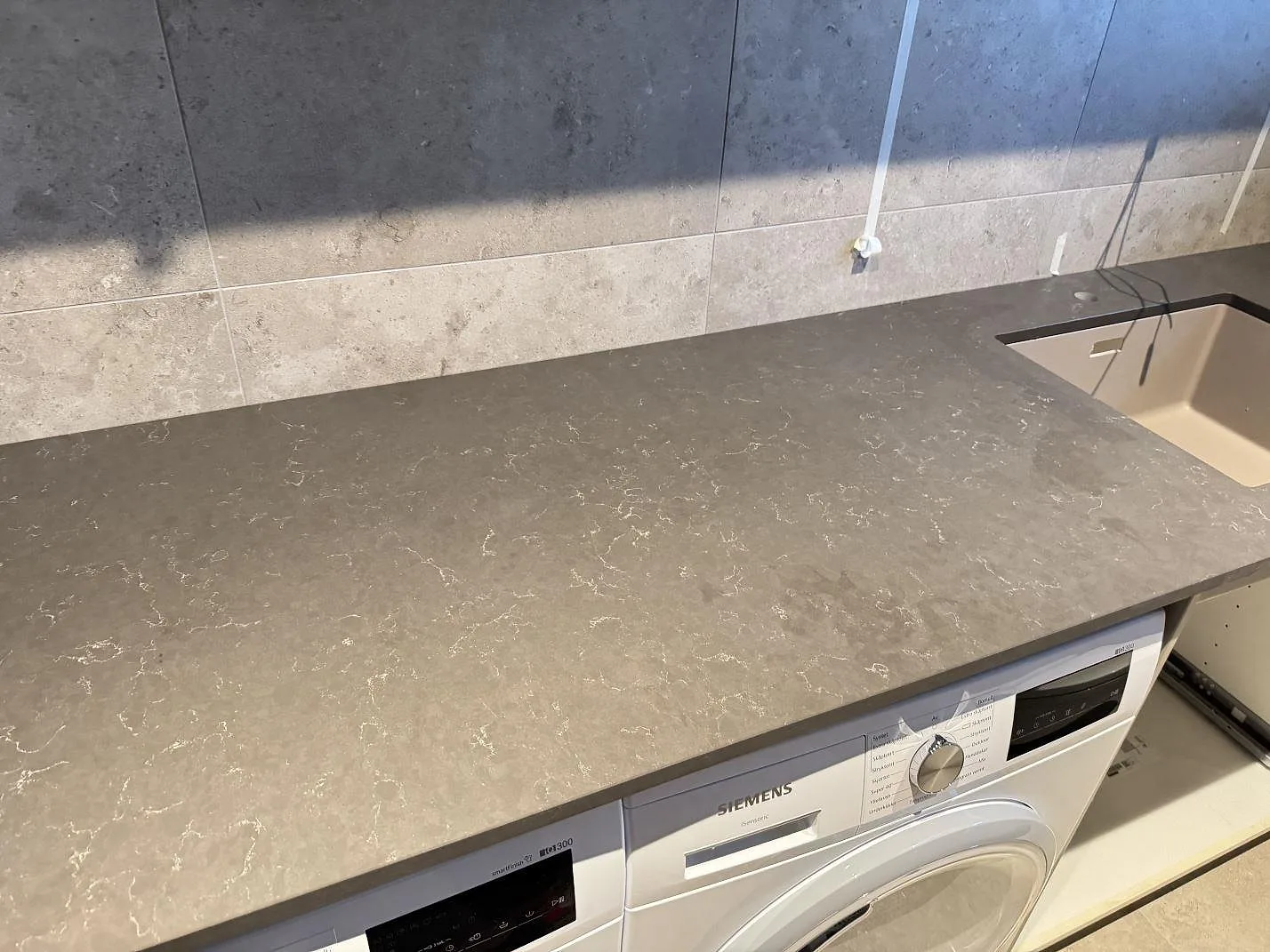 Bordplade i grå Silestone Calypso, mat kvartskomposit, med lys vask og tvättmaskin i ett våtrum i Alingsås.