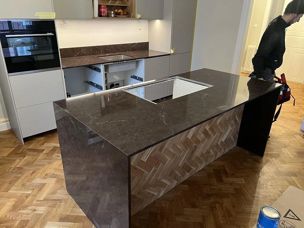 Køkkenø og køkkenbordplade i poleret Silestone Chateau Brown, mörkbrun kompositsten med uppvikt stänkkant i ett køkken i Stockholm.