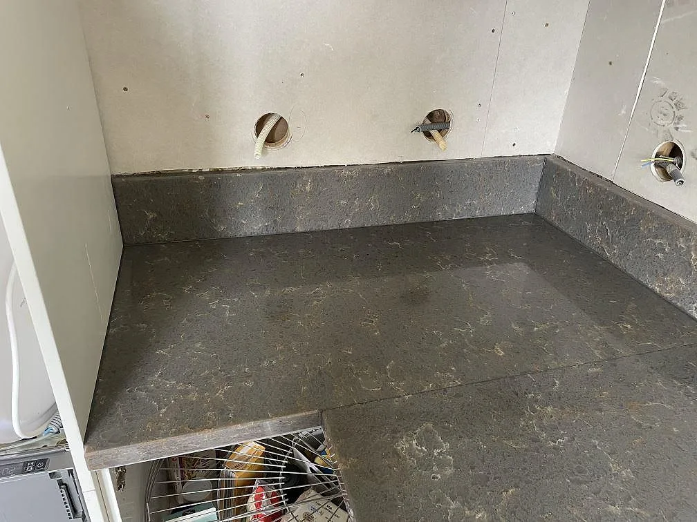 Køkkenbordplade i Silestone Cooper Mist, grå-taupe kvartskomposit med uppvikt stänkkant, i ett køkken under montering i Lerum.
