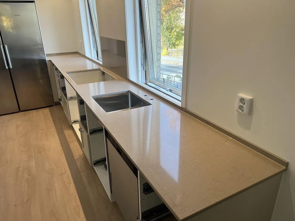 Køkkenbordplade i poleret Silestone Coral Clay i ett køkken i Älvsjö, med diskhozon, låg stänkkant og vindue längs bordpladen.