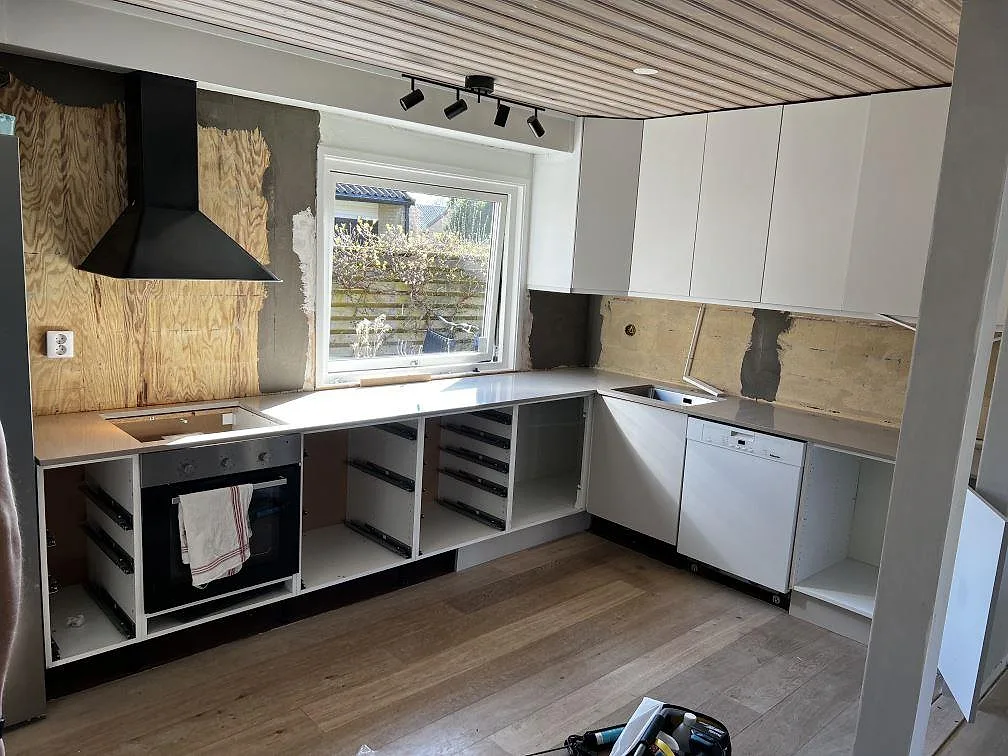 Køkkenbordplade i Silestone Coral Clay, poleret, monteret som L-format køkken rundt om fönstret med udskæring for kogeplade i ett køkken i Bjärred under montering.