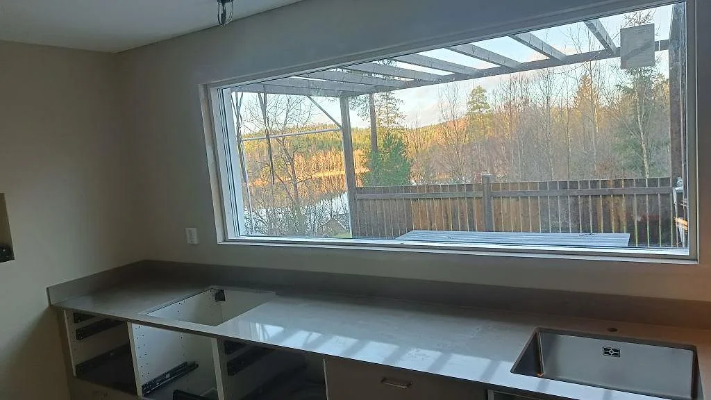 Køkkenbordplade i poleret Silestone Coral Clay, gråbeige kvartskomposit, under ett brett vindue med rostfri vask og stænkplade i Härryda.