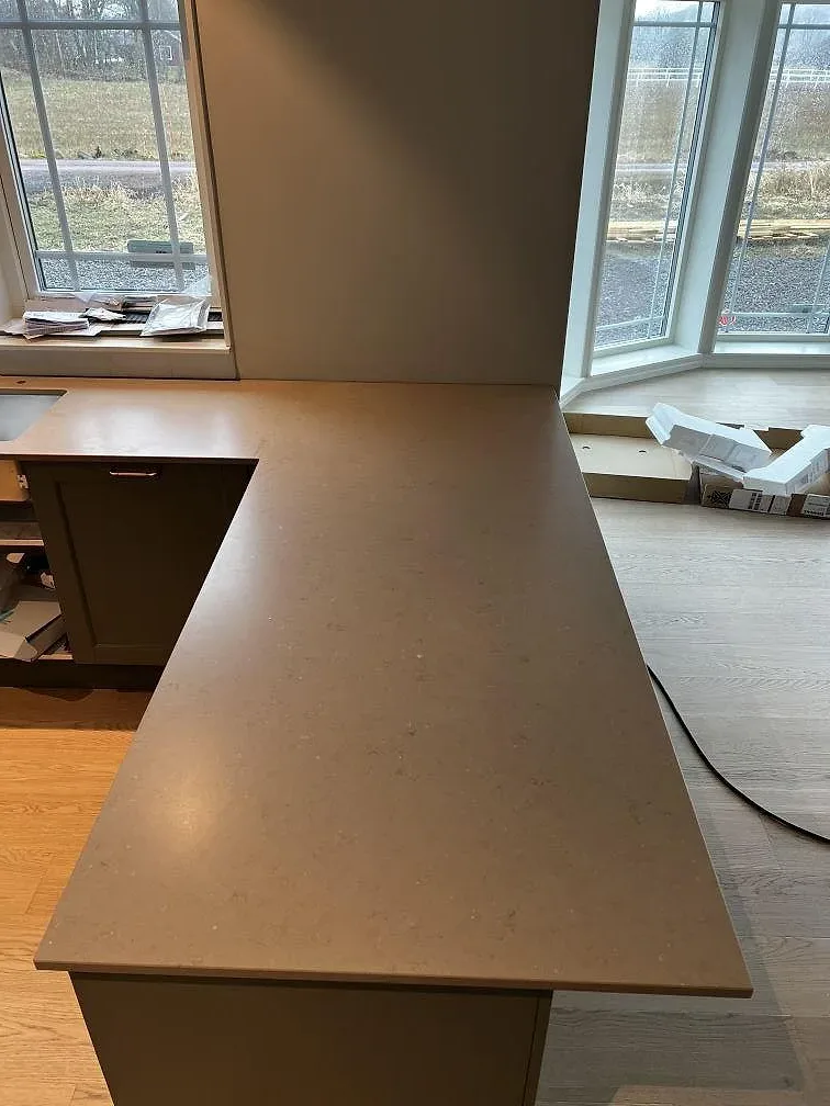Køkkenbordplade og halvö i greige Silestone Coral Clay, mat Suede-overflade, längs ett fönsterparti i ett køkken under montering i Kärna.