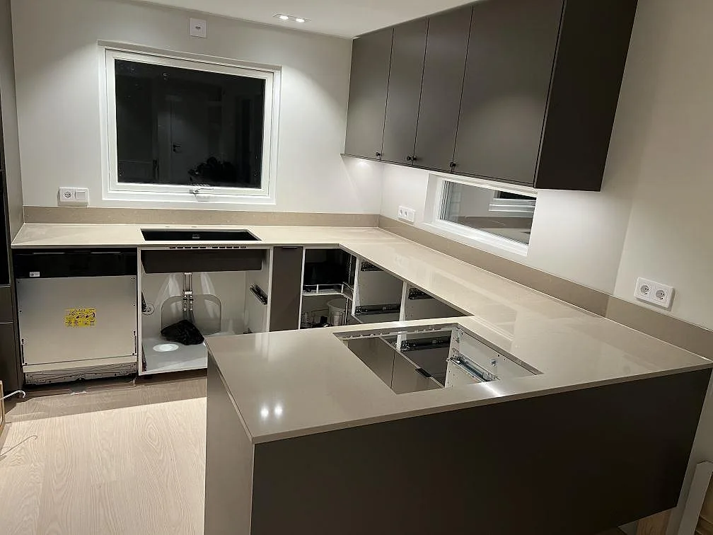 Køkkenbordplade i Silestone Coral Clay, poleret gråbeige kvartskomposit, monteret i U-format køkken med låg stänkkant og hällurtag i Karlskoga.