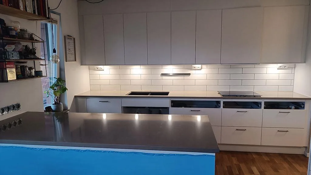 Køkkenbordplade i poleret Silestone Coral Clay, varm gråbeige kvartskomposit, med køkkenø, bänkrad, vask og kogeplade i ett køkken i Limhamn.
